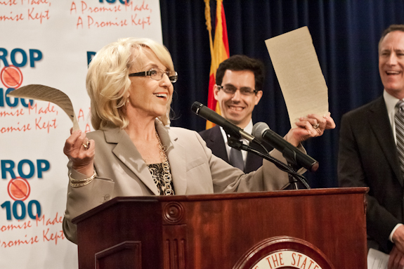 AZ Gov. Jan Brewer tears in half a copy of the bil that enacted a temporary one-cent sales tax in 2010, which Brewer successfully helped pass in 2009. (Photo by Evan Wyloge/Arizona Capitol Times)