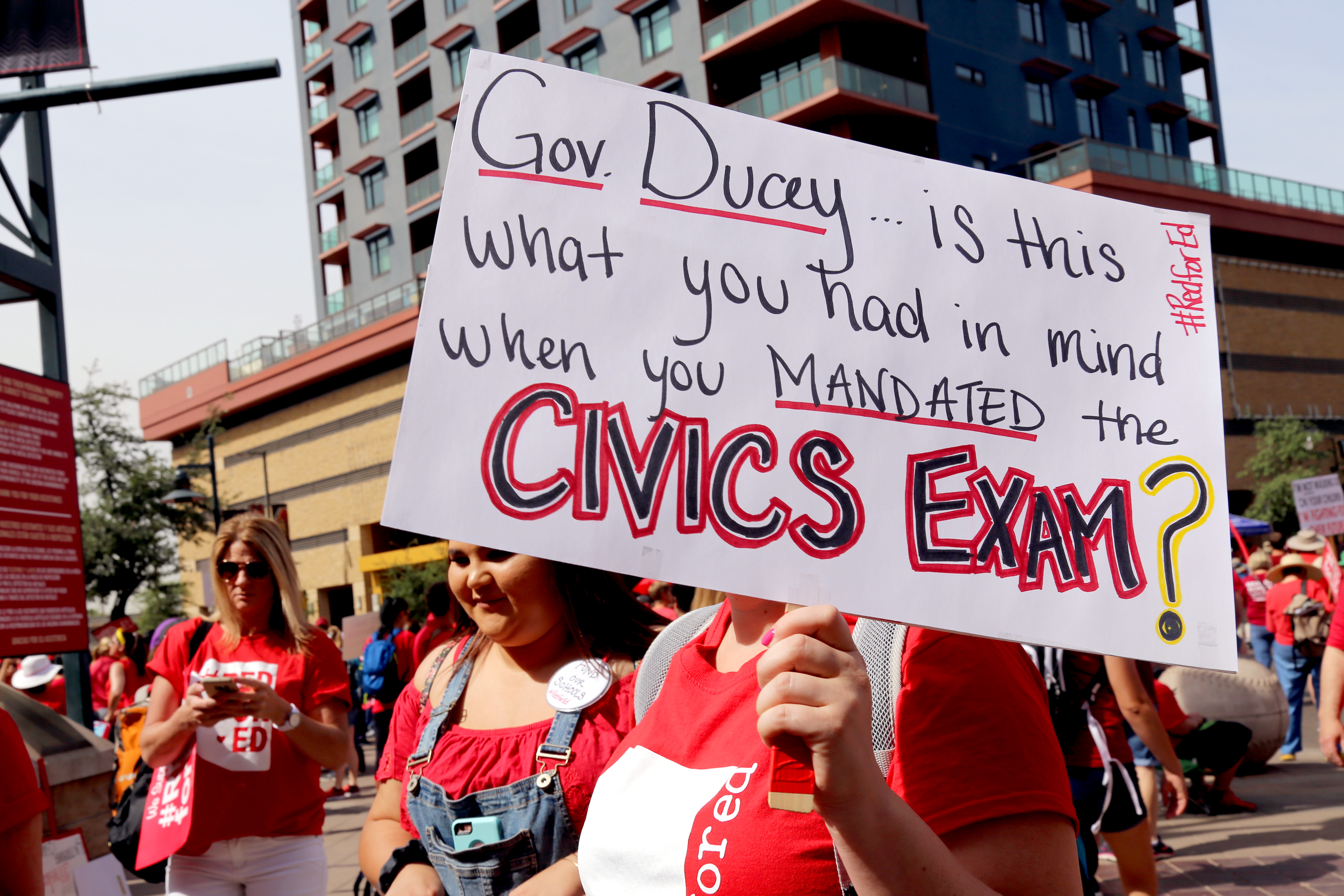 A woman holds a sign that reads "Gov. Ducey... is this what you had in mind when you mandated the civics exam?". She joined thousands of protesters at Chase Field before marching to the Arizona Capitol on April 26. (Photo by Katie Campbell/Arizona Capitol Times)