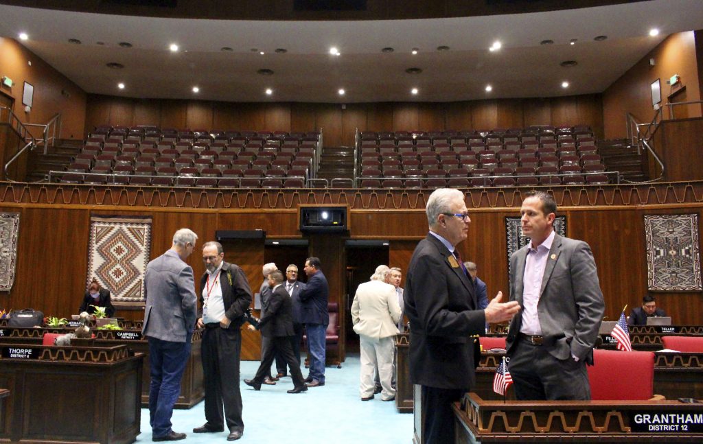 Republican Rep. Noel Campbell, foreground left, speaks with GOP Rep. Travis Grantham, foreground right, as members gather in the Arizona House under a closed public gallery before a floor session at the Capitol in Phoenix, Wednesday, March 18, 2020. The House hopes to quickly pass a bare-bones budget and send it to the Senate before adjourning until the coronavirus crisis ebbs. (AP Photo/Bob Christie)