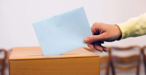 a woman slips a ballot into a ballot box.